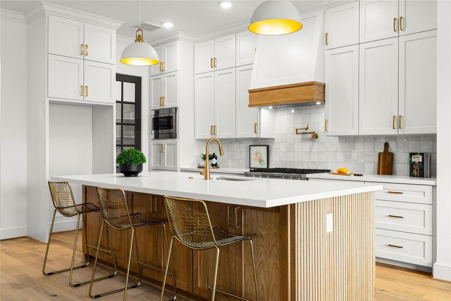 Modern kitchen features a spacious island with quartz countertop, custom cabinetry, and stylish pendant lighting. The wood accents and white oak floors add warmth.