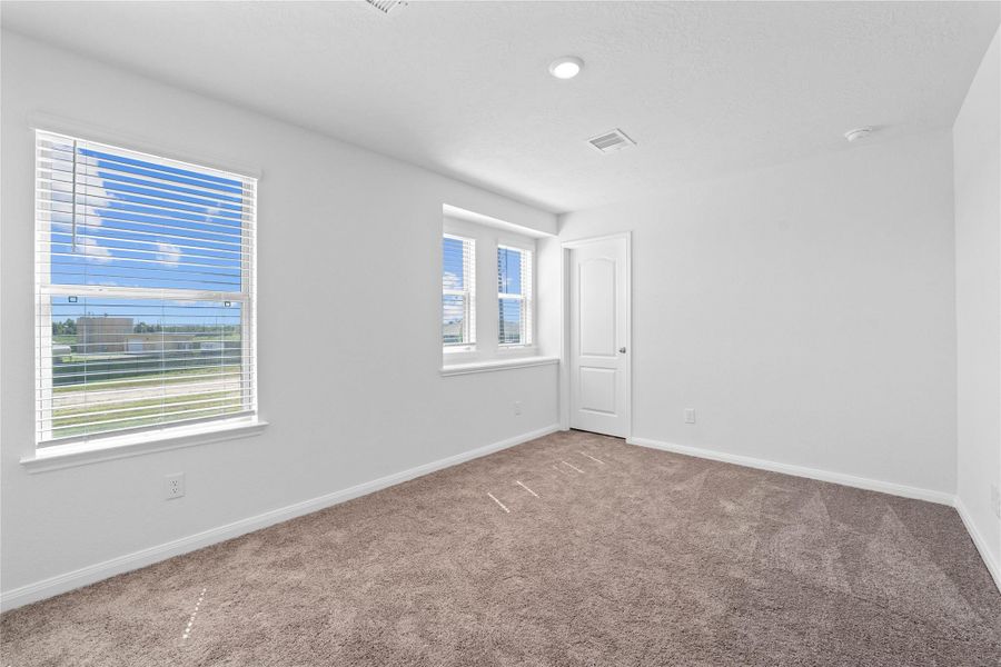 This secondary bedroom offers comfort and style with plush carpeting, neutral paint tones, recessed lighting, a large window with blinds, and a generously sized closet.