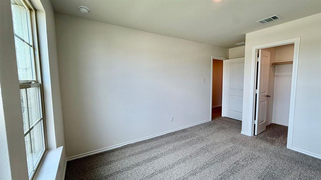 Carpeted interior room featuring a large window, neutral paint, white trim, and a closet with a bi-fold door