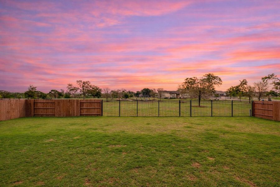 The property features a spacious yard with a well-maintained lawn, partially enclosed by a wooden privacy fence and a black metal fence, offering an expansive view of the surrounding landscape
