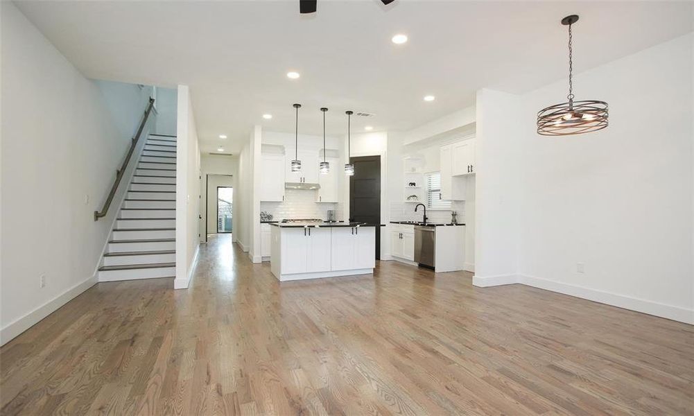 This photo showcases a modern, open-concept living space with hardwood floors, a stylish kitchen with an island and pendant lighting, and a staircase leading to the upper floor. The space is bright with recessed lighting and a contemporary chandelier, offering a clean and inviting atmosphere.