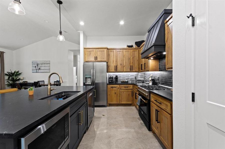 Kitchen with stainless steel appliances, tasteful backsplash, a kitchen island with sink, vaulted ceiling, and decorative light fixtures
