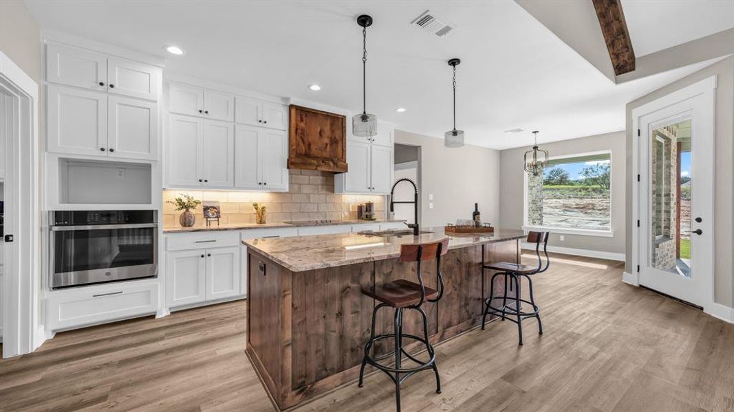 Kitchen with a kitchen island with sink, white cabinetry, and stainless steel oven