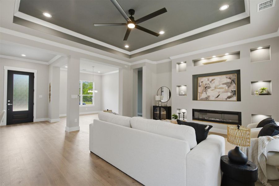 Recessed lighting illuminates the stylish tray ceiling, highlighting the inviting living room with its modern fireplace. Recessed lighting illuminates the stylish tray ceiling, highlighting the inviting living room with its modern fireplace.