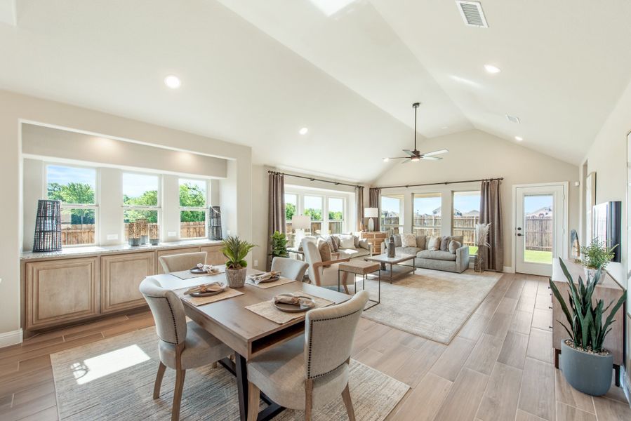 Open-concept dining and living area with vaulted ceiling, hardwood floors, and large windows