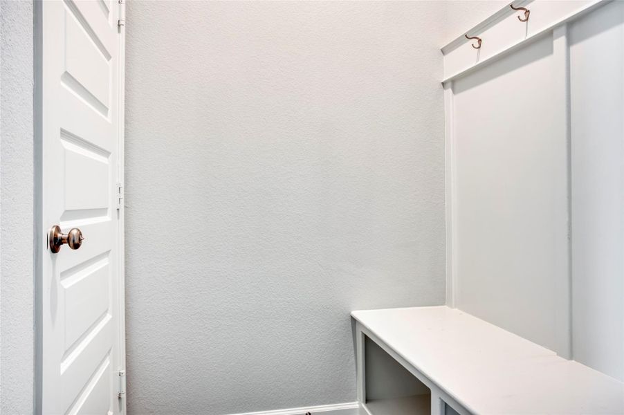 This photo shows a small mudroom area with a simple white bench and coat hooks above, adjacent to a white door. This photo shows a small mudroom area with a simple white bench and coat hooks above, adjacent to a white door.