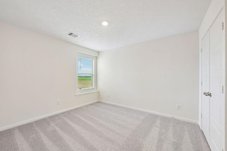 This secondary bedroom offers comfort and style with plush carpeting, neutral paint tones, recessed lighting, large window with blinds, and a generously sized closet.