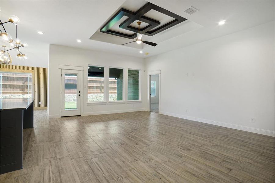 Unfurnished living room featuring coffered ceiling, hardwood / wood-style flooring, and ceiling fan with notable chandelier