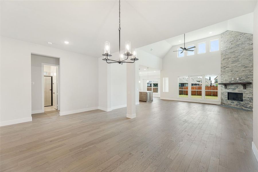 Open living area with vaulted ceiling, stone fireplace, hardwood floors, and chandelier Open living area with vaulted ceiling, stone fireplace, hardwood floors, and chandelier