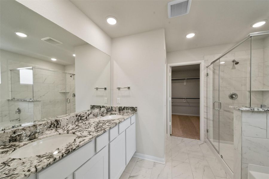 Sophisticated en-suite featuring a double granite vanity, glass-enclosed marble-tile shower, and a spacious walk-in closet.