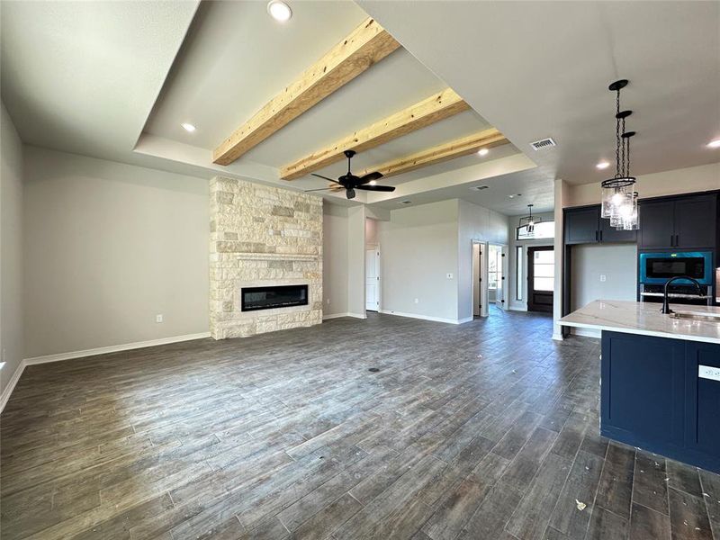 Unfurnished living room featuring recessed lighting, beam ceiling, a ceiling fan, a stone fireplace, and dark wood-style flooring Unfurnished living room featuring recessed lighting, beam ceiling, a ceiling fan, a stone fireplace, and dark wood-style flooring