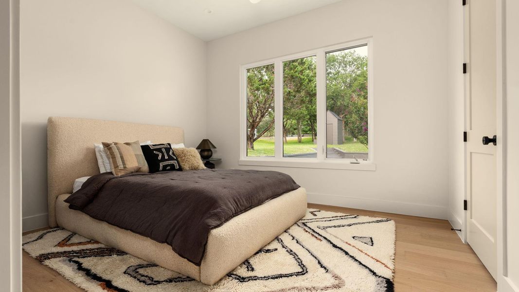 A tranquil primary bedroom with light wood flooring and bright windows. A tranquil primary bedroom with light wood flooring and bright windows.