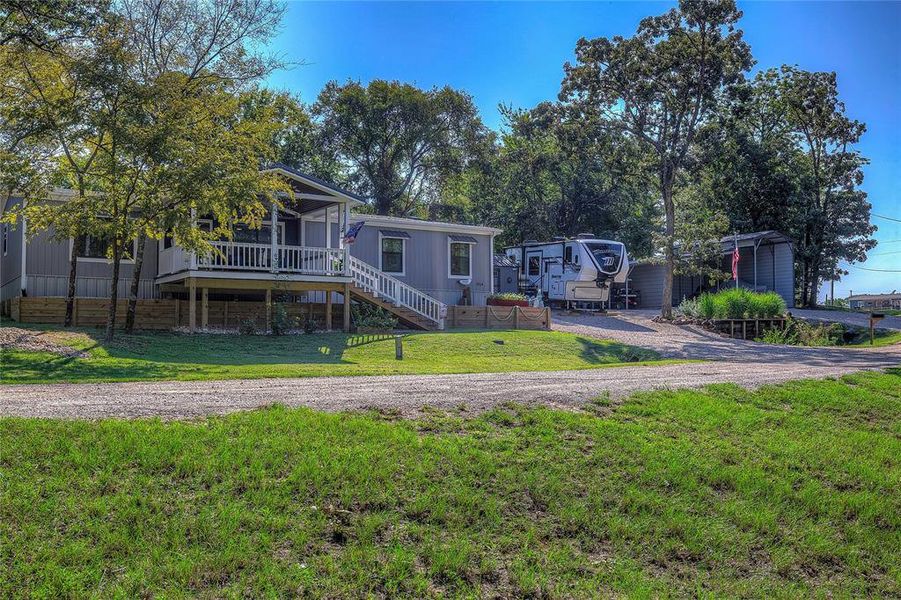 View of front facade with covered front porch, gravel drive, four-car carport, RV parking.
