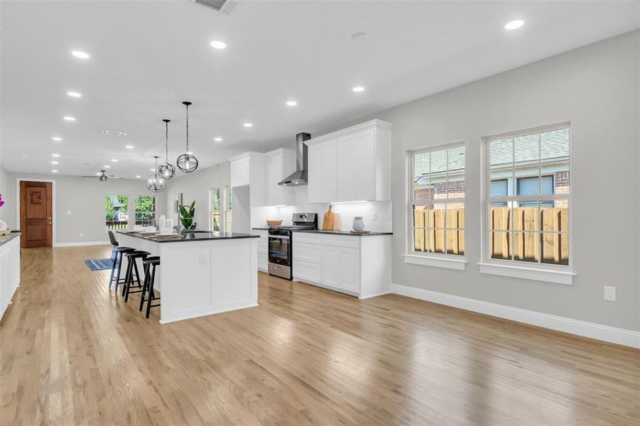 Kitchen with a kitchen breakfast bar, open floor plan, white cabinets, pendant lighting, and stainless steel range