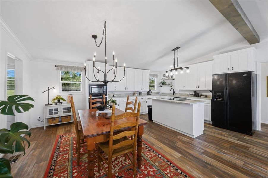 Open-concept kitchen and dining area featuring white cabinetry, black hardware, wood-finish flooring, an island with a light-toned countertop, and two distinct overhead light fixtures