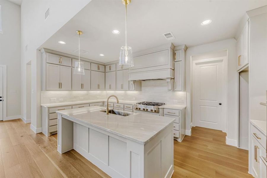 Kitchen featuring a kitchen island with sink, tasteful backsplash, light stone counters, and light wood-type flooring