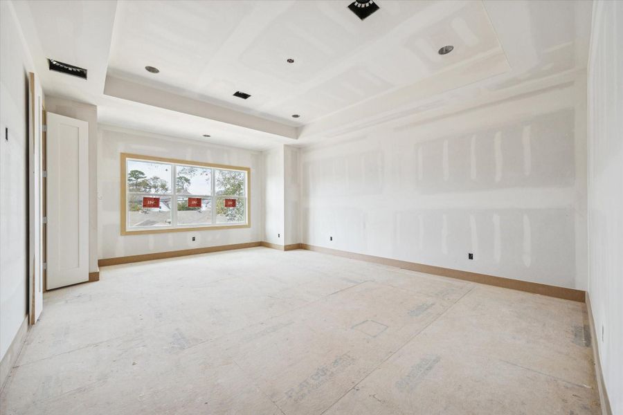 Spacious primary suite with tray ceiling detail and recessed lighting for a refined architectural touch. Oversized window brings in natural light while the generous footprint allows for a true retreat with room for a sitting area.