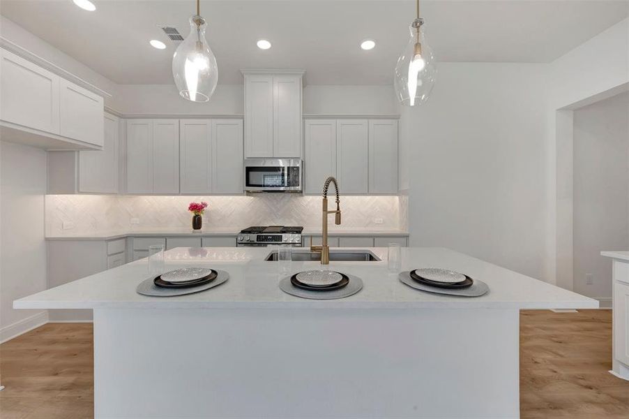 Bright kitchen featuring a large central island with a sink, white cabinetry, integrated stainless steel appliances, and wood-finish flooring
