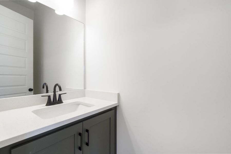 Dark grey shaker-style vanity cabinet with matte black hardware, white solid-surface countertop, integrated rectangular sink, and matte black widespread faucet Dark grey shaker-style vanity cabinet with matte black hardware, white solid-surface countertop, integrated rectangular sink, and matte black widespread faucet