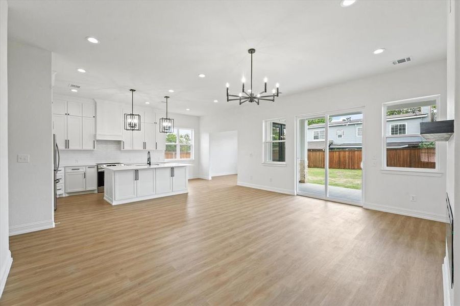 Open-concept living area featuring wood-finish flooring, a contemporary chandelier, recessed lighting, and a sliding glass door to the backyard