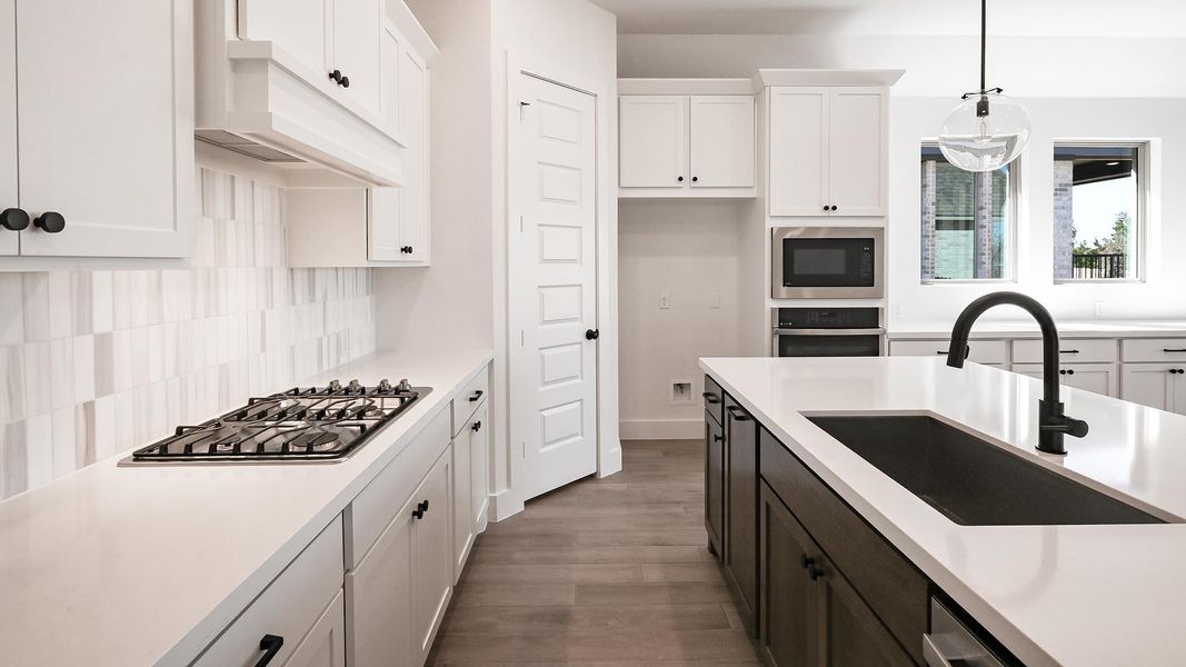 Kitchen with stainless steel appliances, light countertops, premium range hood, white cabinetry, and a sink