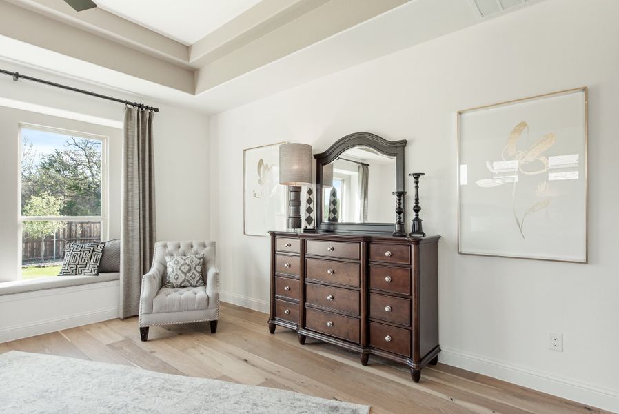 Bedroom with dark wood dresser and mirror, tufted accent chair, window seat, and light hardwood floors Bedroom with dark wood dresser and mirror, tufted accent chair, window seat, and light hardwood floors
