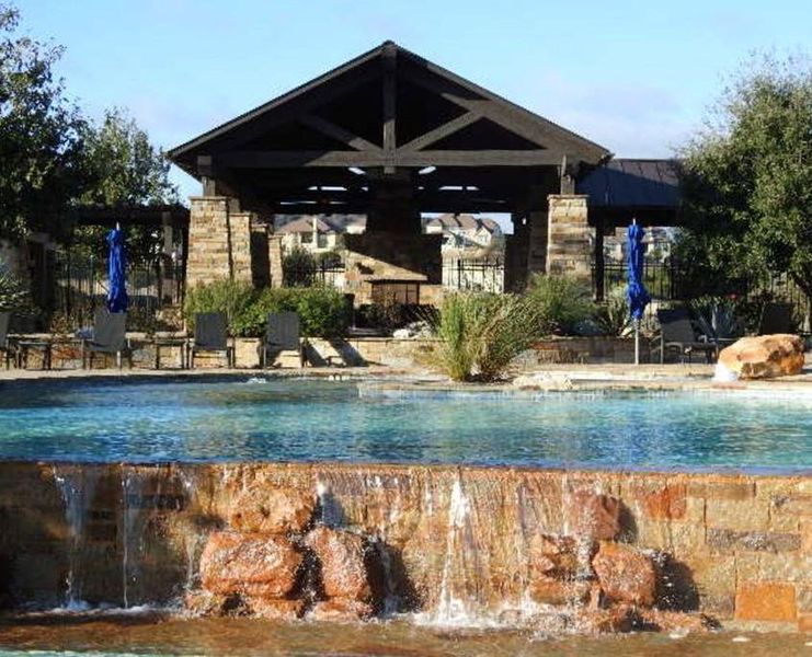 A shimmering pool with a stone waterfall feature complements the inviting shaded patio structure.