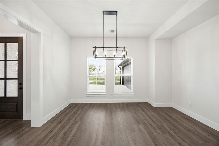 Spacious interior room featuring wood-finish flooring, a modern linear chandelier, and crisp white walls