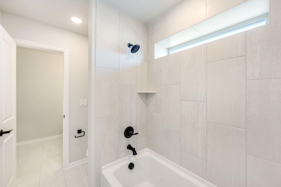 Bathroom with soaking tub, large tile surround, black fixtures, and a narrow window above the tub Bathroom with soaking tub, large tile surround, black fixtures, and a narrow window above the tub