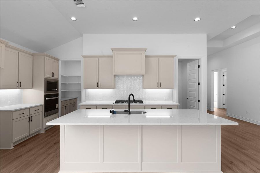 Kitchen featuring cream cabinets, tasteful backsplash, light stone countertops, recessed lighting, and vaulted ceiling