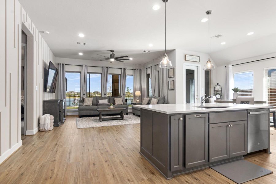 This open-concept living area features a modern kitchen with a large island and sleek cabinetry, flowing into a spacious living room with floor-to-ceiling windows offering plenty of natural light and views of the outdoors. The hardwood floors and recessed lighting add a touch of elegance, creating a welcoming and stylish space.