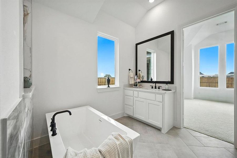 Bathroom with a freestanding bath, vanity, light tile patterned flooring, and lofted ceiling