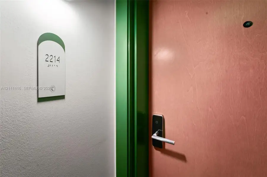 Entryway featuring a wood-finish door, high-contrast green trim, electronic keyless entry system, and wall-mounted unit signage