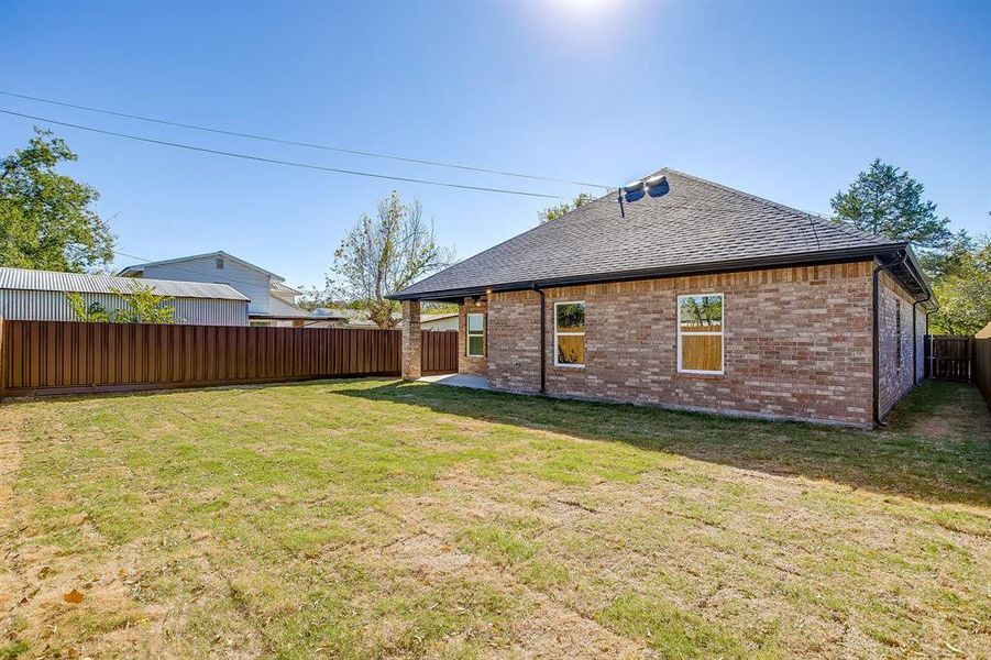 Rear view of property featuring a patio area, a fenced backyard, roof with shingles, and brick siding