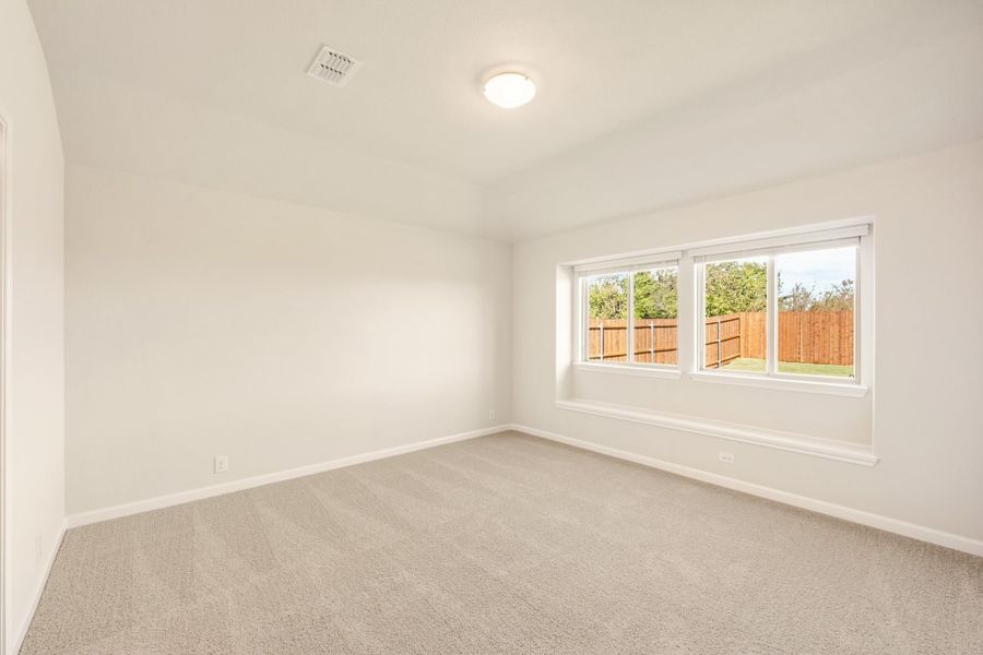 Empty bedroom with beige carpet, white walls, and a large window overlooking a fenced backyard
