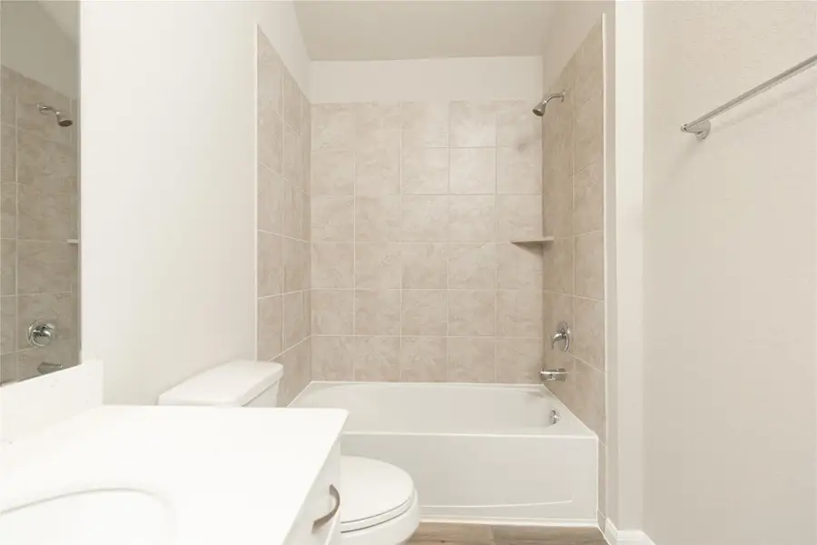 Secondary bath features tile flooring, bath/shower combo with tile surround, light stained wood cabinets, beautiful light countertop. Sample photo of completed home with similar floor plan. Actual colors and selections may vary.