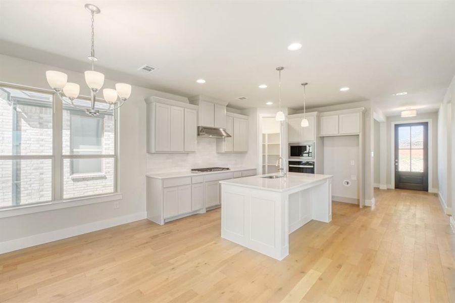 Kitchen featuring a center island with sink, hanging lights, white cabinets, light wood-style floors, and stainless steel appliances