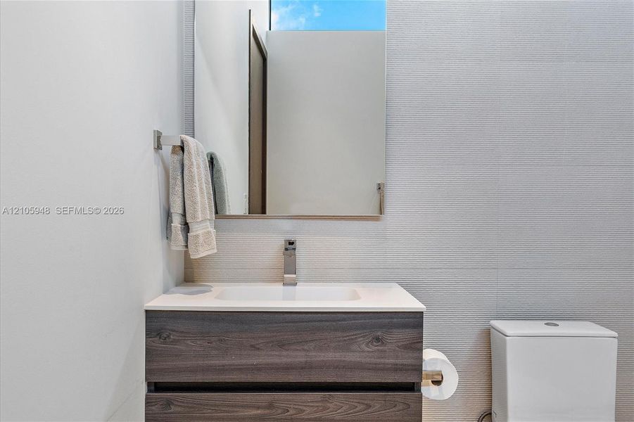 Floating vanity with a wood-finish, dual-drawer cabinet, crisp white countertop, integrated sink, and modern polished metal faucet, complemented by a large frameless mirror and textured wall tiling