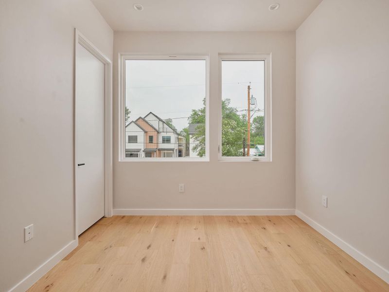 Room featuring wood-finish flooring, two large windows, white trim, recessed lighting, and a solid core door with contemporary hardware
