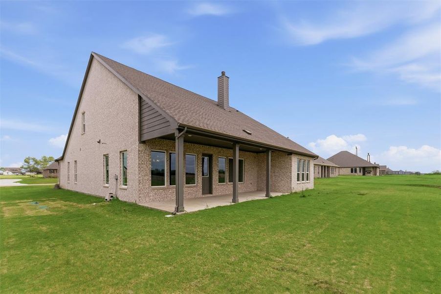 Back of property with a lawn, a chimney, a patio, and brick siding