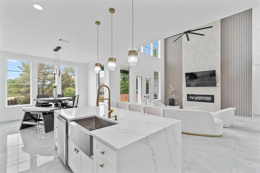 Spacious open-concept interior featuring a kitchen island with a farmhouse sink, contemporary pendant lighting, a dining area with expansive windows, a living area with a fireplace, and a striking accent wall