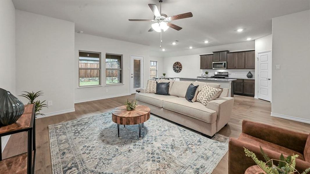 Open-concept living area featuring wood-finish flooring, a contemporary ceiling fan, recessed lighting, and ample natural light from multiple windows
