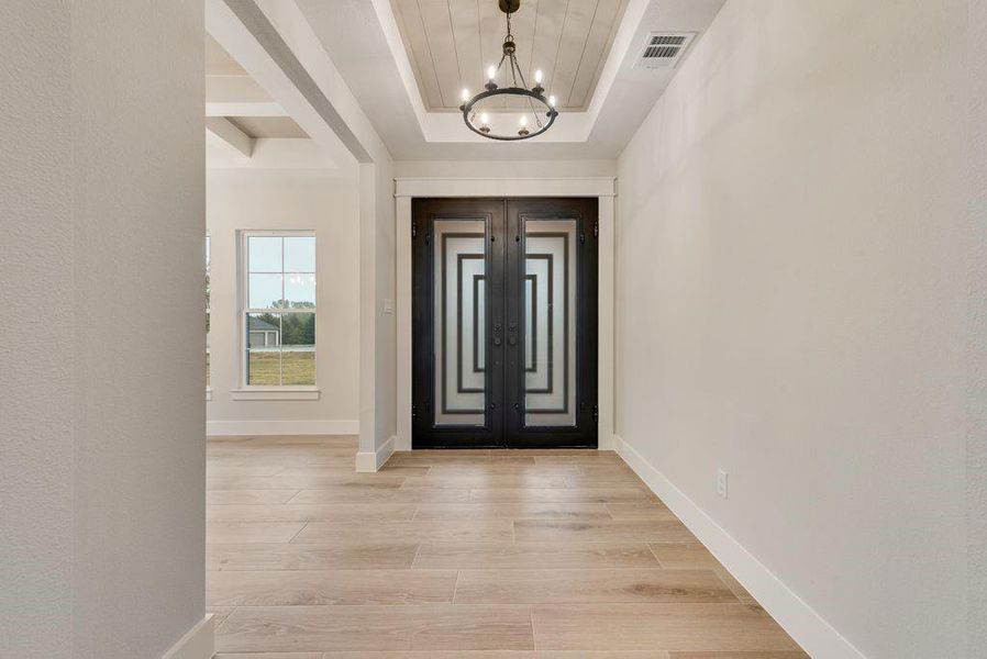 Foyer with french doors, light hardwood / wood-style floors, a chandelier, and a tray ceiling