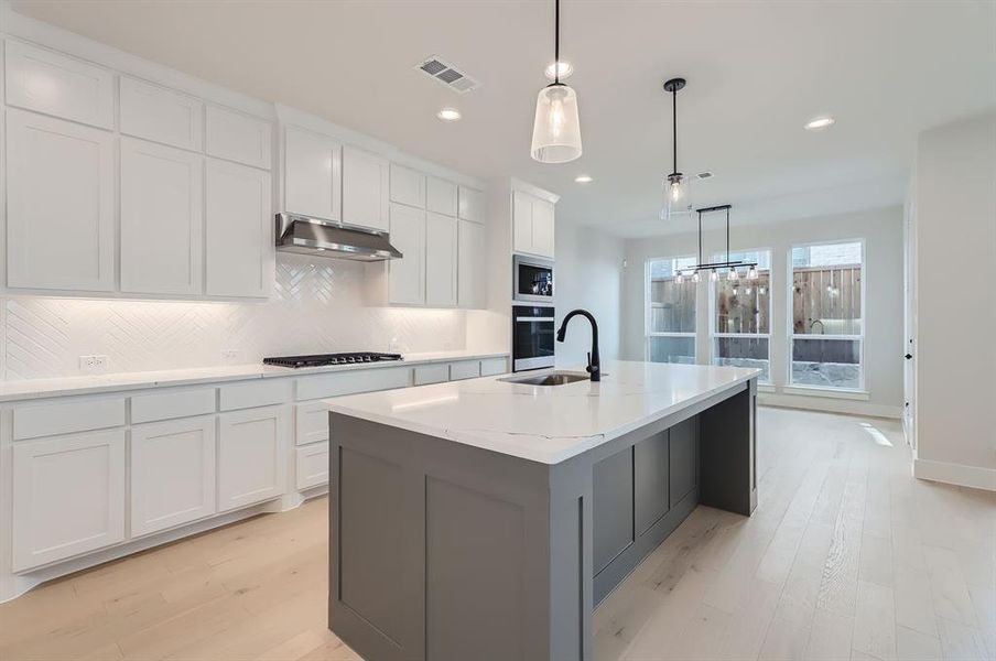 Kitchen with hanging light fixtures, a center island with sink, white cabinets, light wood-type flooring, and appliances with stainless steel finishes