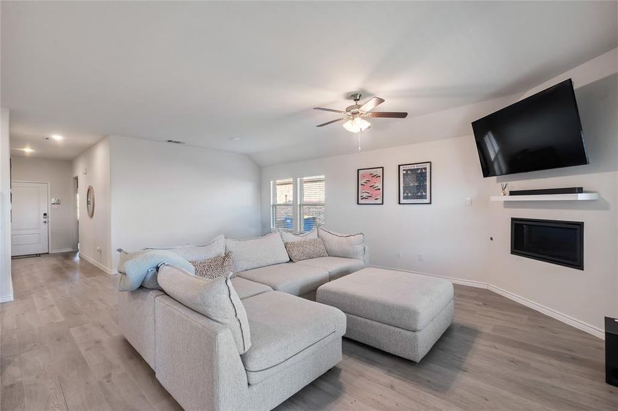 Living area featuring a glass covered fireplace, light wood finished floors, and a ceiling fan