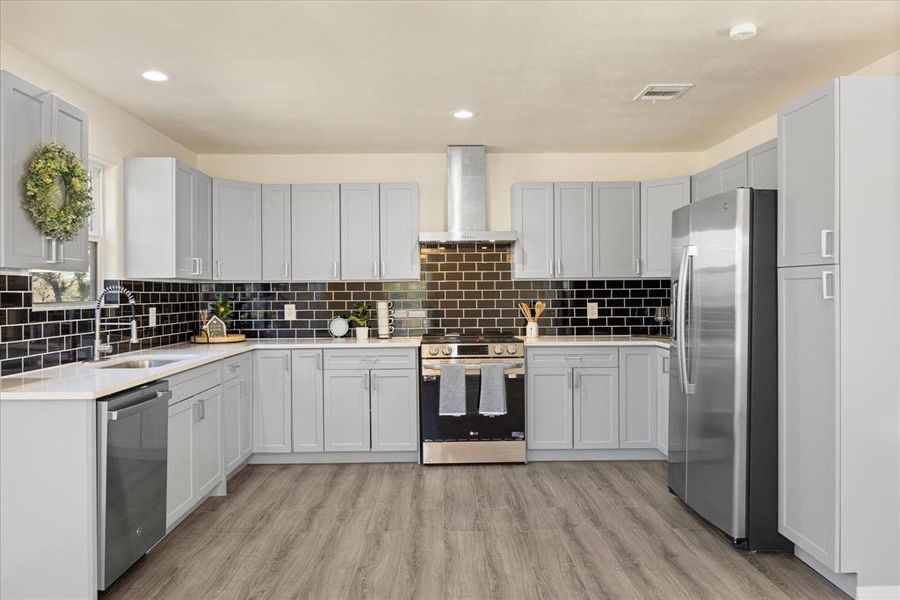 Kitchen with appliances with stainless steel finishes, tasteful backsplash, sink, light hardwood / wood-style floors, and wall chimney exhaust hood