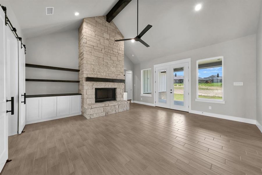 featuring light hardwood / wood-style floors, a fireplace, ceiling fan, a barn door, and cathedral beam ceiling