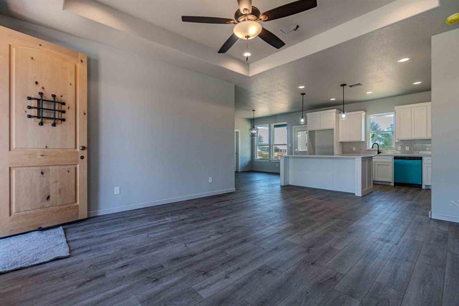 Unfurnished living room featuring a tray ceiling, dark wood-style flooring, ceiling fan, and recessed lighting Unfurnished living room featuring a tray ceiling, dark wood-style flooring, ceiling fan, and recessed lighting