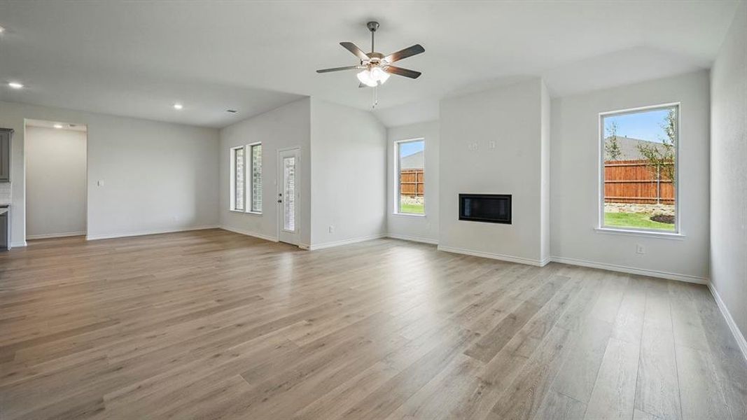 Unfurnished living room featuring a glass covered fireplace, light wood finished floors, plenty of natural light, and a ceiling fan