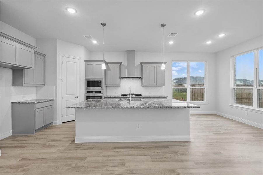 Kitchen with gray cabinets, stainless steel appliances, wall chimney range hood, light stone countertops, and recessed lighting